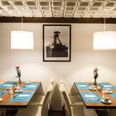 A stylish restaurant interior features neatly set tables with blue placemats and flowers under modern pendant lights.