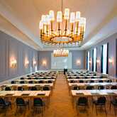 A spacious, elegant conference room is set up with rows of tables and chairs under grand chandeliers for a formal event.