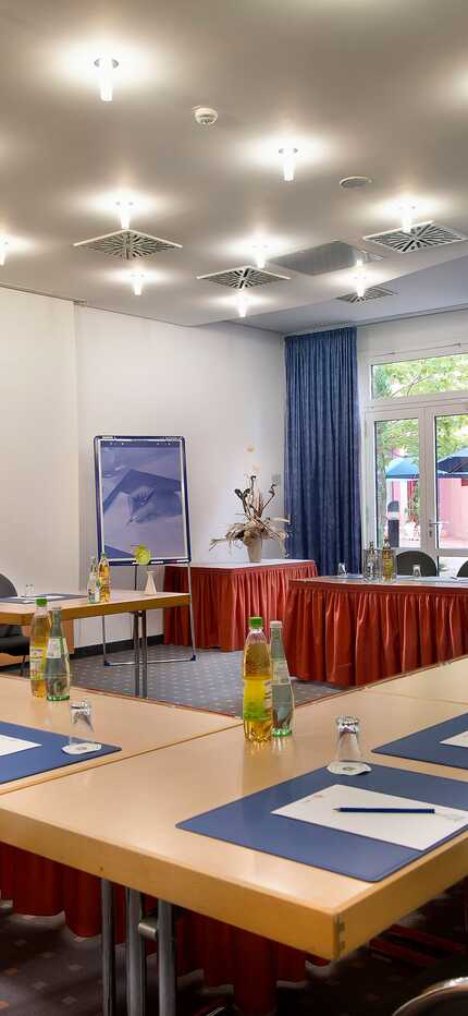 A spacious meeting room with a U-shaped table setup, featuring blue notepads and bottled water for attendees.
