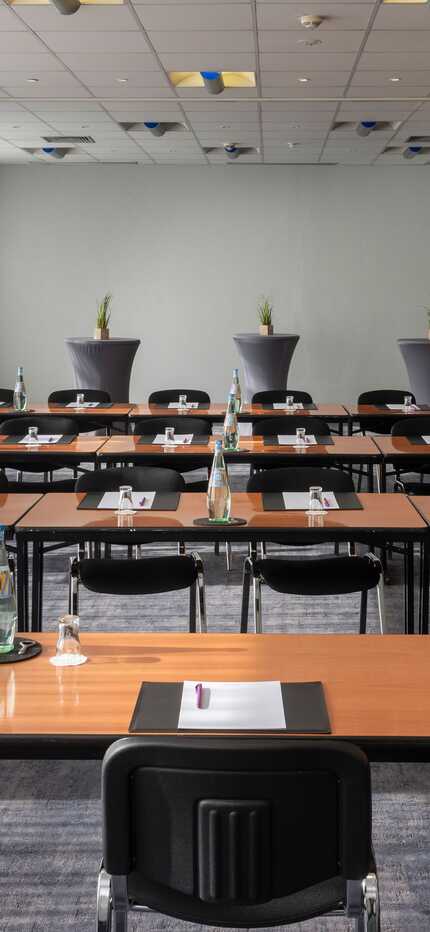 Ein Konferenzraum ist für eine Tagung vorbereitet, mit Tischen, Stühlen, Wasserflaschen und Schreibmaterial.