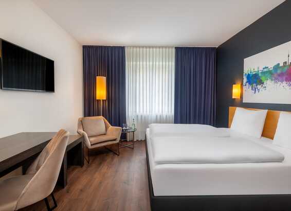 Ein modernes Hotelzimmer mit einem Doppelbett, einem Schreibtisch und einem bunten Bild an der Wand bietet Komfort und Stil.