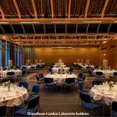 An elegant banquet hall with round tables set for an event, adorned with candles and floral centerpieces under twinkling lights.