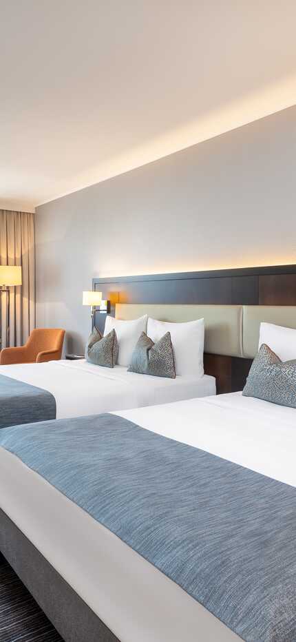 Ein modernes Hotelzimmer mit zwei Doppelbetten, einem Schreibtisch und einem großen Fenster sorgt für eine entspannte Atmosphäre.