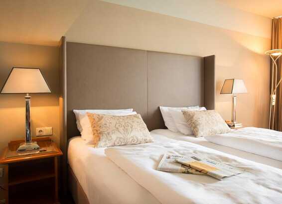 Ein gemütliches Hotelzimmer mit zwei Einzelbetten, dekorativen Kissen und Nachttischen mit stilvollen Lampen.