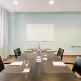 A modern conference room features a sleek table set with glasses and notepads under soft lighting.