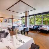 Elegant club room with neatly set tables, surrounded by art and a view of lush greenery through large windows.