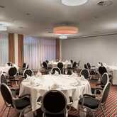 A banquet hall is elegantly set with round tables, white tablecloths, and neatly arranged chairs, ready for a formal event.