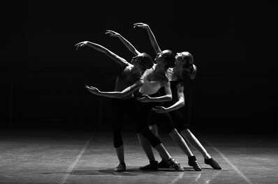 Three ballerinas gracefully pose in unison on stage, their arms elegantly extended in a dramatic dance formation.