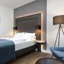 Modern eingerichtetes Hotelzimmer mit gemütlichem Bett, stilvoller Stehlampe und abstrakten Kunstwerken an der Wand.