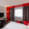 A modern hotel room features vibrant red accents, a comfortable bed, and a sleek workspace with a TV and chair.