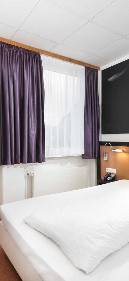 Ein modernes Einzelzimmer mit einem gemütlichen Bett, einem Schreibtisch und einem großen Blumenbild an der Wand.
