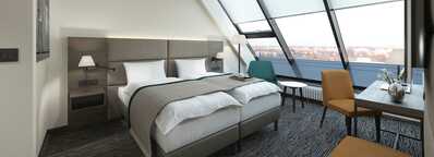 A modern hotel room with a double bed, stylish decor, and large windows offering a panoramic view of the city.