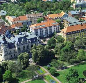 An aerial view showcases a historic hotel surrounded by lush greenery and charming buildings.