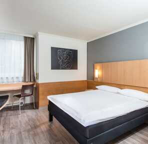 Ein modernes Einzelzimmer mit einem gemütlichen Bett, Schreibtisch und stilvoller Kunst an der Wand.