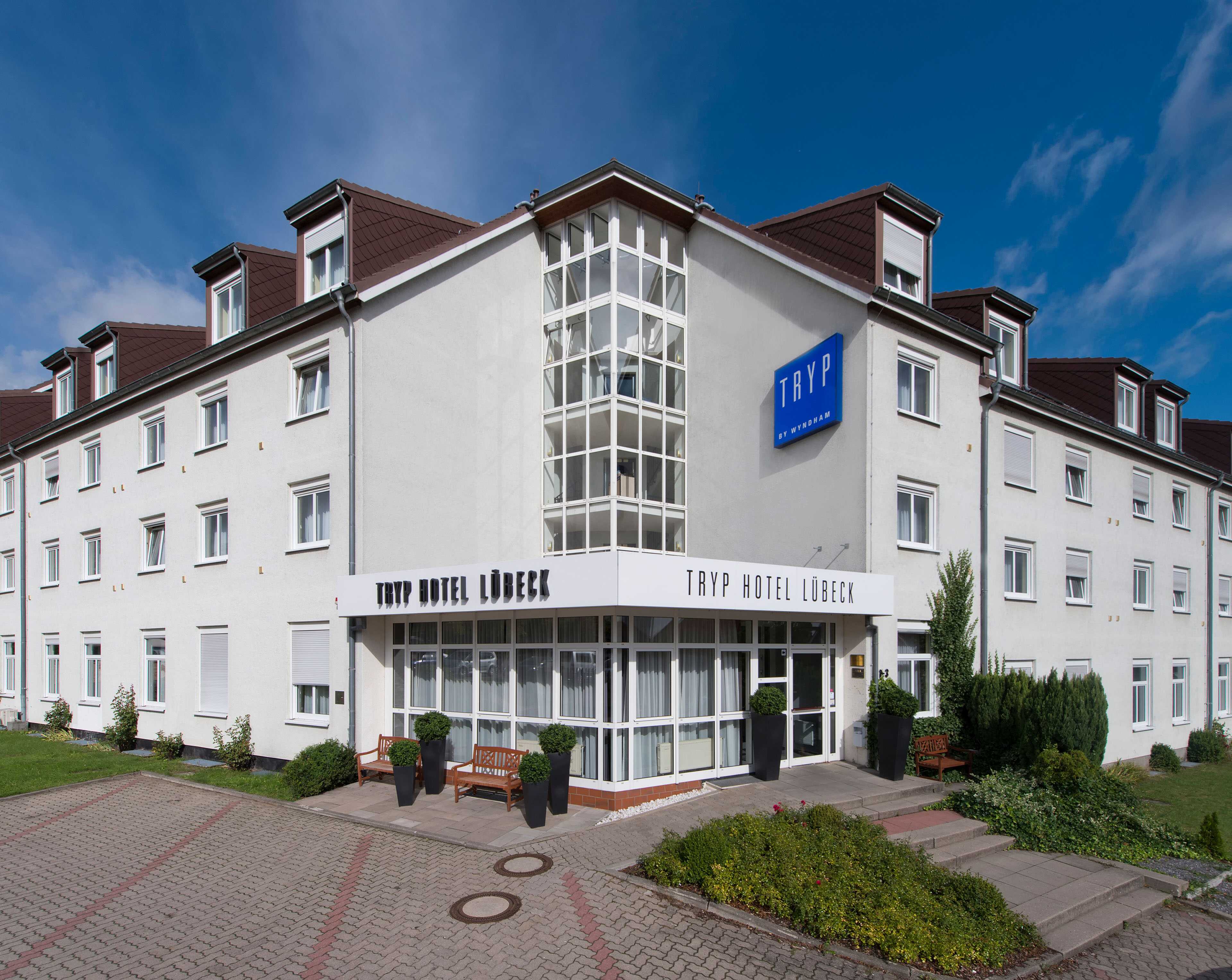 The exterior of Tryp Hotel Lübeck features a modern facade with large windows and a welcoming entrance under a clear sky.