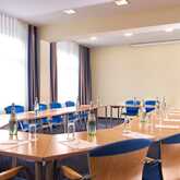 Ein heller Konferenzraum mit U-förmiger Tischanordnung, blau gepolsterten Stühlen und bereitgestellten Wasserflaschen.