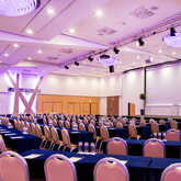 A spacious conference room with rows of chairs and tables is prepared for an upcoming event under elegant lighting.
