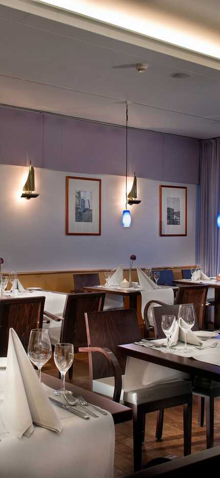 A cozy restaurant features elegantly set tables with folded napkins and warm lighting, creating an inviting dining atmosphere.