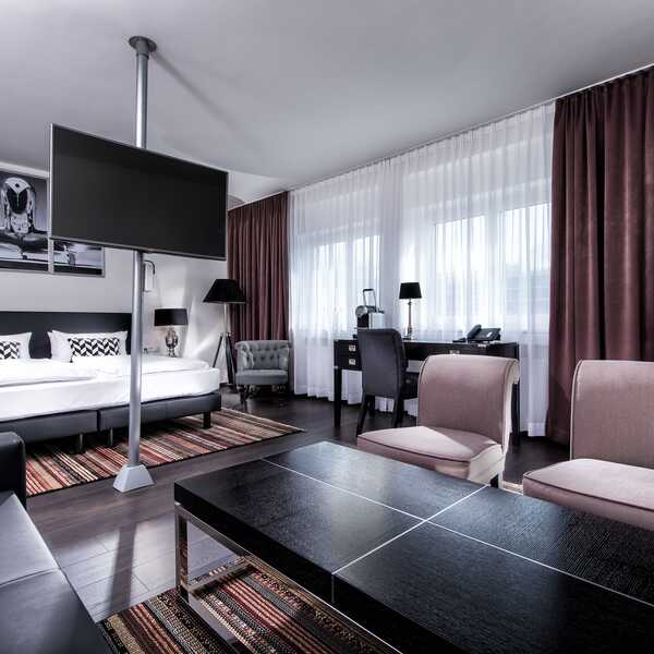 Moderne Suite mit stilvollen Möbeln, einem großen Bett und einem Flachbildfernseher, der zentral im Raum steht.