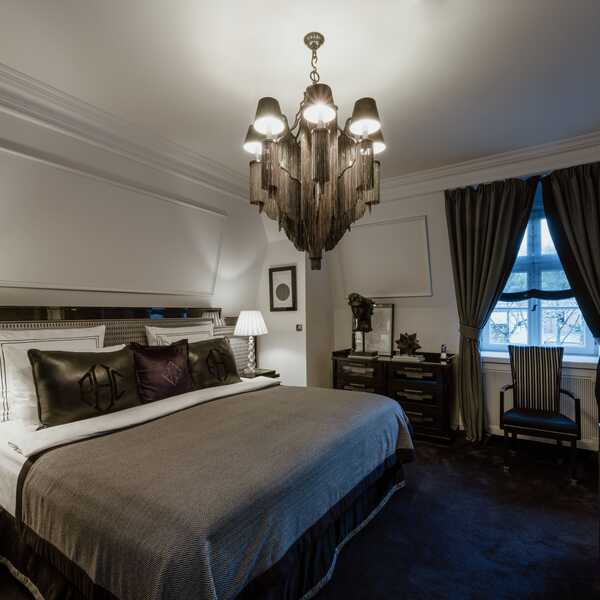 Eine elegante Premium Junior Suite mit luxuriösem Bett, stilvoller Beleuchtung und einem Fenster mit schweren Vorhängen.