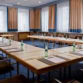 Ein Konferenzraum mit U-förmig angeordneten Tischen ist für ein Meeting mit Wasserflaschen und Gläsern vorbereitet.