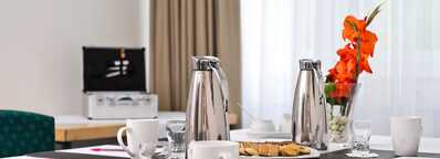 A well-set meeting room table with coffee pots, mugs, and a vase of orange flowers, ready for a conference at Georgengarten.