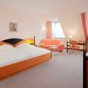A spacious double room features a cozy bed, peach sofa, and a TV, creating a comfortable retreat.