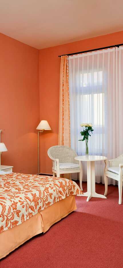 Gemütliches Zimmer mit einem großen Bett, einem kleinen Tisch mit zwei Stühlen und einem beruhigenden grünen Kunstwerk an der Wand.