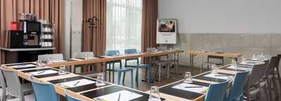 A conference room is set up with a U-shaped table arrangement, complete with notepads, pens, and glasses for a meeting.