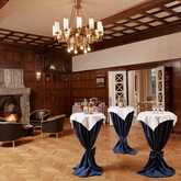 A cozy room with a lit fireplace, elegant chandeliers, and tables set for a formal gathering creates a warm ambiance.