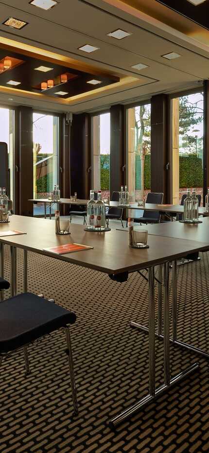 A modern meeting room setup at the Wasserturm hotel with a large table and chairs, surrounded by floor-to-ceiling windows.