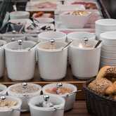 An array of breakfast options with cereals and pastries is artfully arranged beside stacked bowls and utensils.
