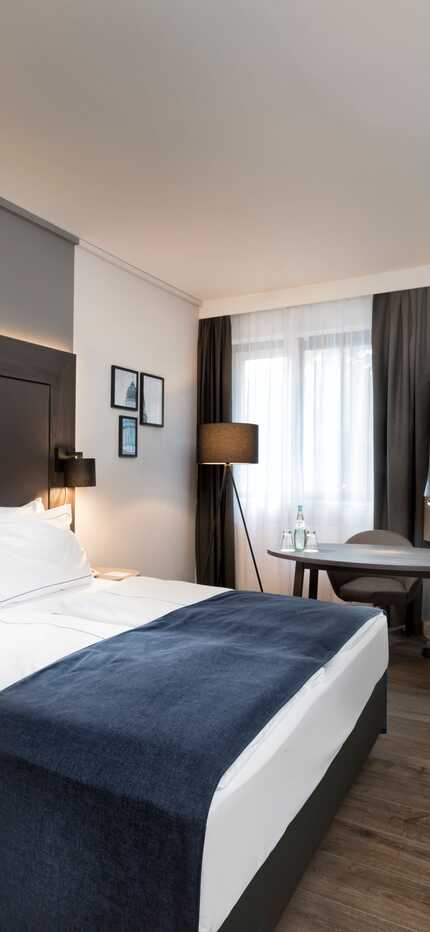 A modern business room features a queen-size bed, sleek furniture, and a wall-mounted TV for a comfortable stay.