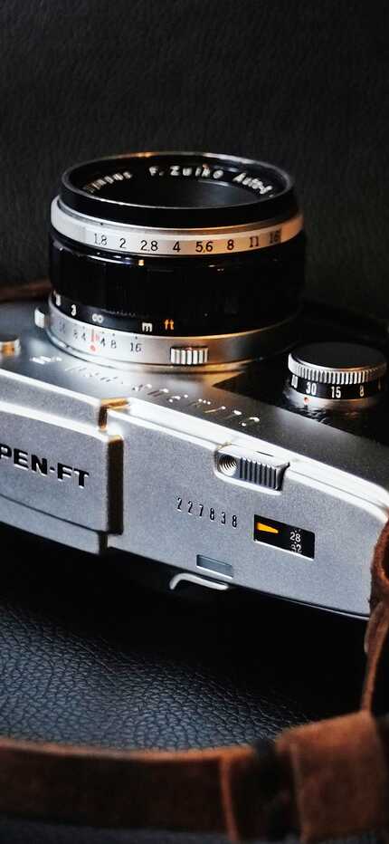 A vintage PEN-FT camera with a leather strap rests on a dark surface, showcasing its classic design.