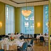 Elegant tables set for a festivity in a bright room with large windows and a stunning chandelier.