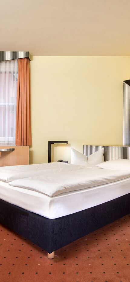 A cozy double room features a comfortable bed, a desk with a chair, and modern decor in warm tones.