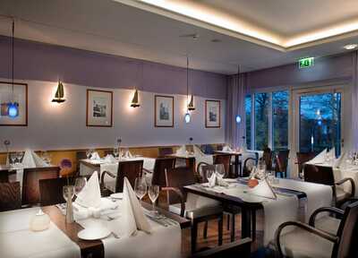 Elegantes Restaurant mit stilvoll gedeckten Tischen, modernen Leuchten und Blick auf den abendlichen Garten durch große Fenster.