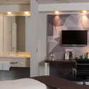 Moderne Business-Zimmer mit Schreibtisch, Fernseher und Badezimmer im Hintergrund.