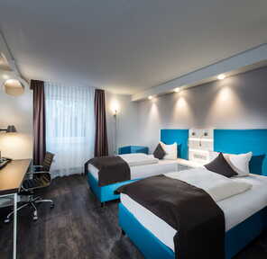 Moderner Twin-Bed-Raum mit zwei Betten, Schreibtisch und HDTV in stilvollem Design.
