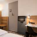 A modern double room features a cozy bed, sleek desk, wall-mounted TV, and contemporary decor.
