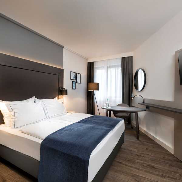 Ein stilvoll eingerichtetes Business-Zimmer mit einem Queen-Size-Bett, einem Schreibtisch und einem großen Flachbildfernseher.