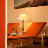 Two orange lounge chairs with drinks sit under a warm lamp, creating a relaxing wellness ambiance.