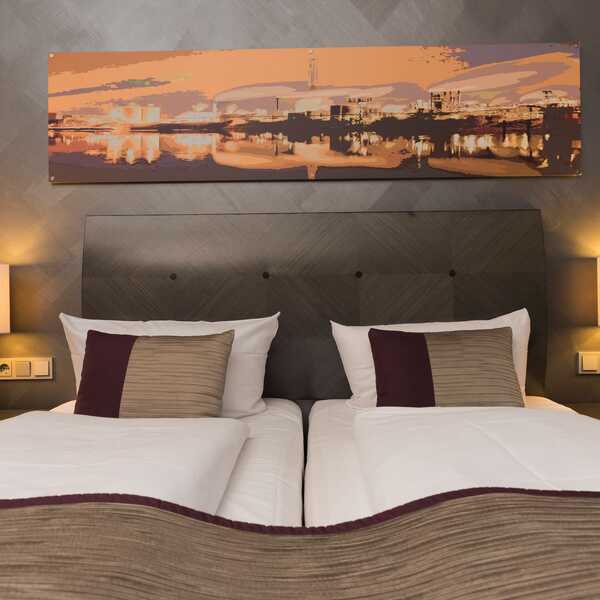 A deluxe hotel room features two neatly made beds, warm lighting, and a cityscape painting above the headboard.