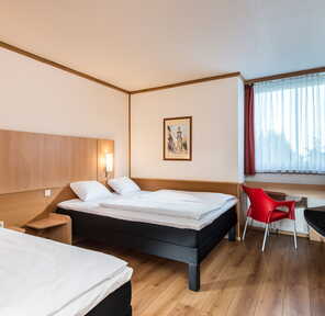 Ein gemütliches Schlafzimmer mit zwei Betten, einer roten Stuhl und einem Fenster, das Tageslicht hereinlässt.