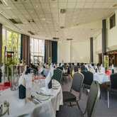 A spacious event hall is elegantly set up for a festivity with round tables, white tablecloths, and floral centerpieces.