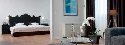 A modern suite features a cozy bedroom with a stylish bed and a sitting area with a table and orchid.