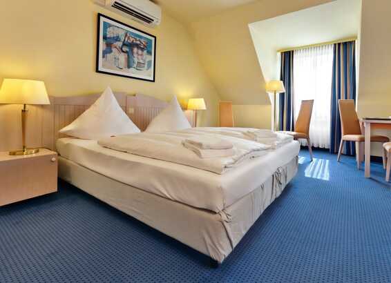 Ein gemütliches Doppelzimmer mit einem großen Bett, zwei Nachttischen und einem Schreibtisch im sonnigen Ambiente.
