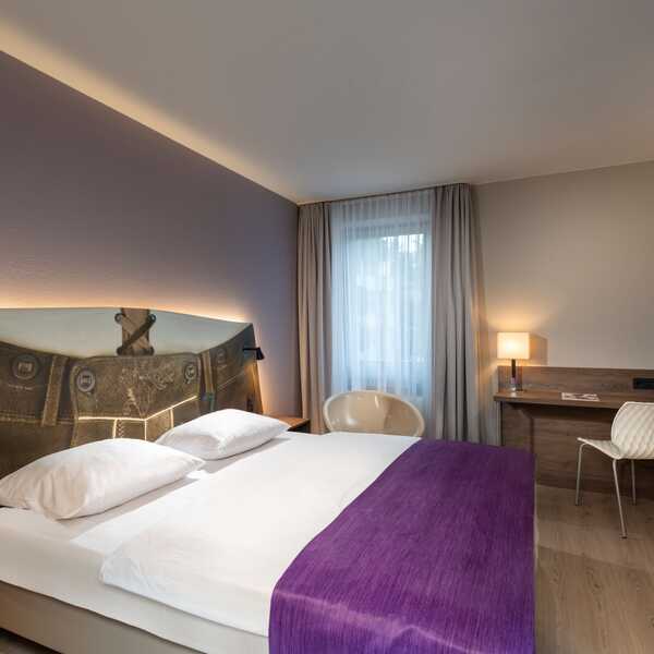 Ein modernes Doppelzimmer mit lila Akzenten und stilvollem Schreibtisch bietet eine einladende Atmosphäre.