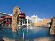 Ein moderner Wasserpark mit großen Rutschen und einem Pool vor einem markanten Gebäude bei strahlend blauem Himmel.