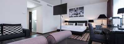 A modern hotel suite features a cozy bed, elegant decor, and a seating area with stylish furnishings.